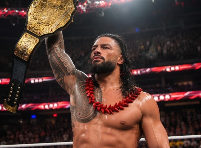 Roman Reigns hält den Weltmeister-Titel im Ring hoch.