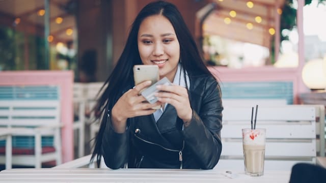 Frau mit einem Smartphone und einer Zahlungskarte in der Hand. Deutschland erhöht Einsatzlimit für Online Slots neue Glücksspielregeln 2026.