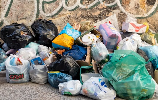 Mülltüten stapeln sich vor einer Hauswand auf der Straße.