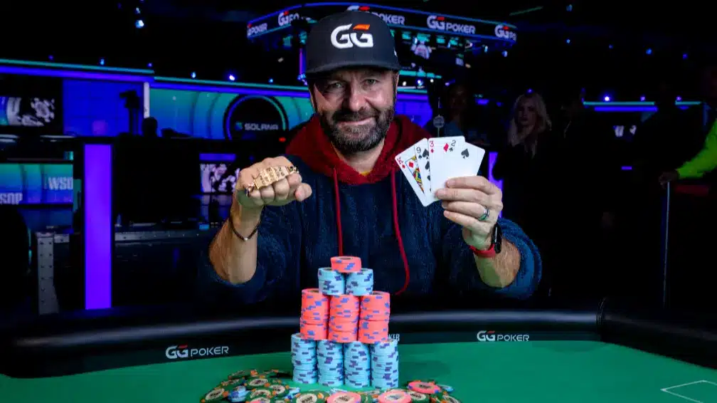 Daniel Negreanu holding WSOP bracelet and playing cards at a poker table with chips.