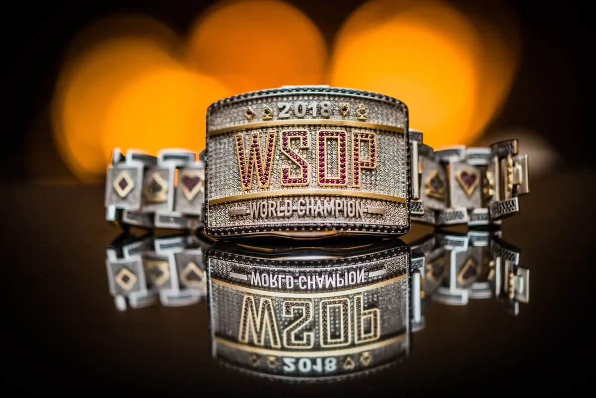 Close-up of a WSOP gold bracelet with red and gold design reflecting on a surface.