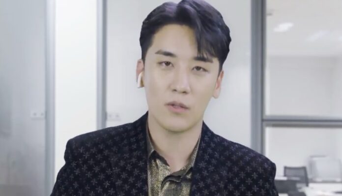 승리 사무실로 보이는 공간에서 짙은 무늬 재킷을 입은 남성이 카메라를 정면으로 바라보고 있는 모습