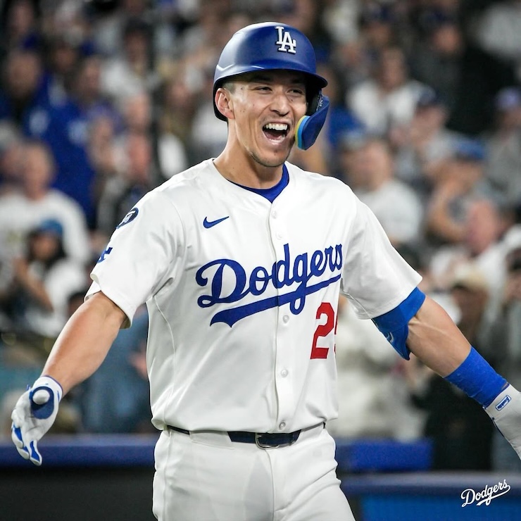 야구 경기장에서 흰색 유니폼과 헬멧을 착용한 선수가 입을 벌린 채 환호하며 두 팔을 벌리고 있는 모습. 관중석이 흐릿하게 보인다.