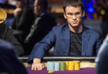 코인포커 $2,500/$5,000 스테이크 오픈, 카이한 모크리 vs. ATAKA 격돌 안경을 쓴 남성이 파란 재킷과 어두운 티셔츠를 입고 포커 테이블에 앉아 있으며, 앞에 여러 색상의 포커 칩이 쌓여 있다. 그는 진지한 표정으로 테이블을 바라보고 있고, 주변에는 다른 플레이어들이 흐릿하게 보인다.