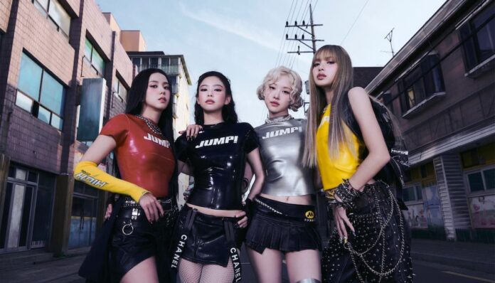 블랙핑크 멤버들이 도심 골목을 배경으로 강렬한 콘셉트의 무대 의상을 입고 나란히 서 있는 모습, 네 명 모두 카메라를 응시하며 카리스마 있는 분위기를 연출하고 있다.