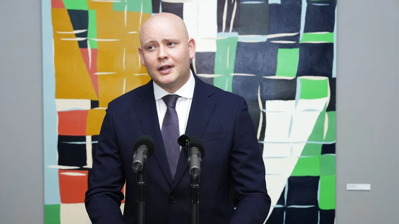 Portrait of Jakob Engel-Schmidt in a dark blue suit and tie speaking at a podium with microphones.