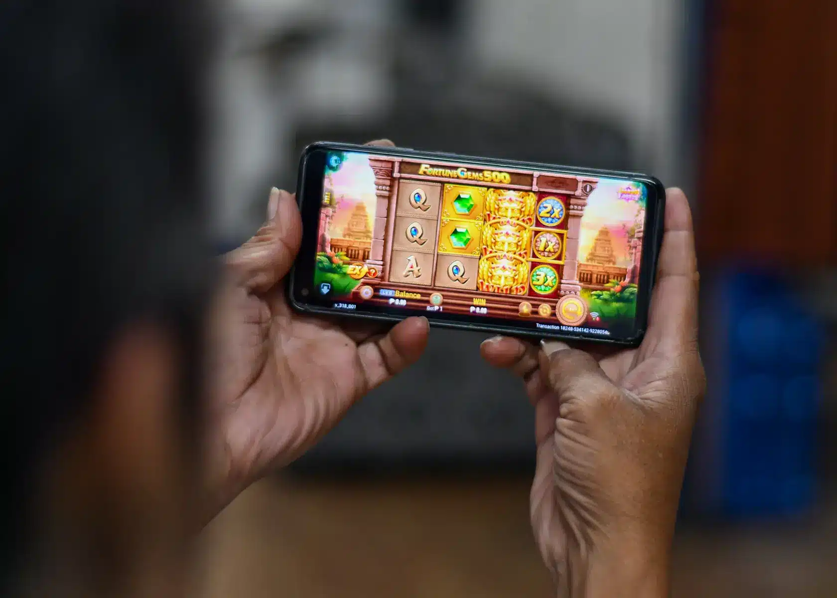 Close-up of hands holding a smartphone displaying an online slot machine game called Fortune Gems 500