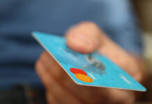 En hand håller ett blått betalkort med Mastercard-logotypen synlig i hörnet.