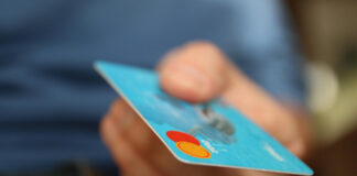 En hand håller ett blått betalkort med Mastercard-logotypen synlig i hörnet.