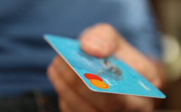 En hand håller ett blått betalkort med Mastercard-logotypen synlig i hörnet.