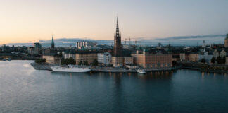 Vy över Riddarholmen i Stockholm med Riddarholmskyrkan och vatten i förgrunden vid skymning.