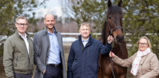 Fyra personer står utomhus tillsammans med en häst, leende mot kameran.