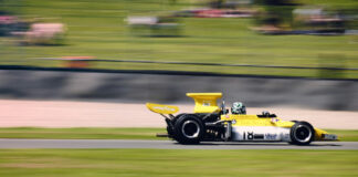 En gulsvart Formel 1-bil kör snabbt på en racerbana med suddiga gröna omgivningar i bakgrunden.