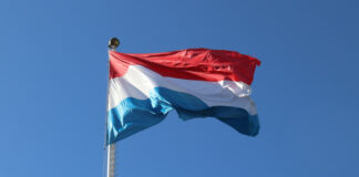 Flagga med horisontella ränder i rött, vitt och blått vajar mot en klarblå himmel.