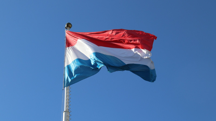 Flagga med horisontella ränder i rött, vitt och blått vajar mot en klarblå himmel.