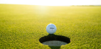 Golfboll nära hål på en solig green, med texten "Titleist 3" synlig på bollen.