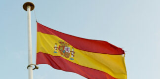 Spaniens flagga vajar i vinden mot en blå himmel.