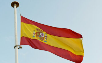 Spaniens flagga vajar i vinden mot en blå himmel.