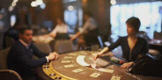 Två personer spelar kort vid ett kasinobord i en stämningsfull och upplyst spelmiljö.