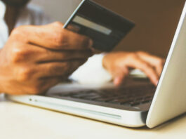 En person gör ett köp online med kreditkort framför en laptop.