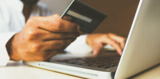 En person gör ett köp online med kreditkort framför en laptop.