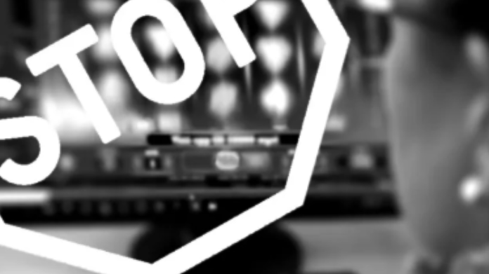 spelinspektionen-stoppar-två-bolag Person vid dator med slots på skärmen, överlagt STOP-tecken i vitt, suddig bakgrund.