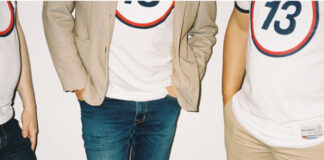 Tre personer i vita t-shirts med siffran 13, en har beige kavaj, armarna nedsänkta vid sidorna.