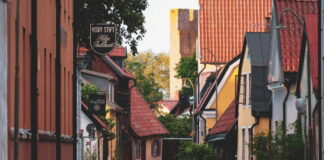 En smal gata i Visby med färgglada hus, röda tak och en kyrktorn i bakgrunden.