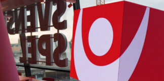 Kub med Svenska Spel-logotyp inomhus, glasvägg i bakgrunden och stadsmiljö utanför.