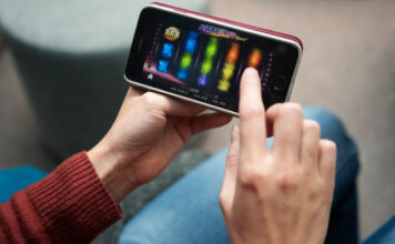 Person spelar en färgglad slot på mobiltelefon i ett avslappnad hemmamiljö.