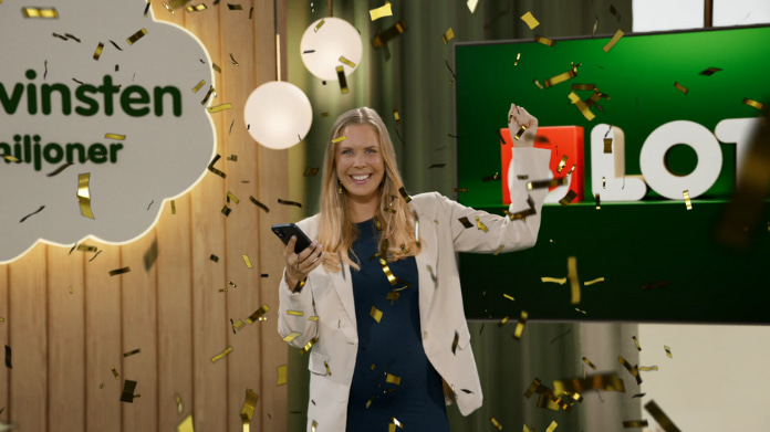 Leende kvinna firar vinst med konfetti framför Lotto-logotyp och skylten ”Drömvinsten”.