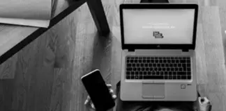 Person använder laptop och mobil vid ett bord, sedd ovanifrån i svartvitt.