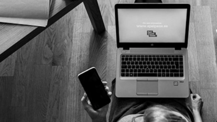 Person använder laptop och mobil vid ett bord, sedd ovanifrån i svartvitt.
