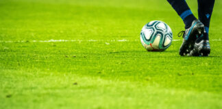 Fotbollsspelare i rörelse på grön plan med bollen nära fötterna.