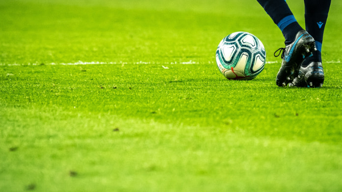 Fotbollsspelare i rörelse på grön plan med bollen nära fötterna.