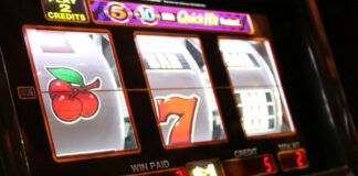 Närbild på en spelautomat med körsbär och sjua på hjulen samt belyst display.