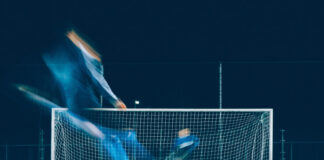 Fotbollsspelare tar sats för att skjuta straff mot mål under kvällsbelysning.