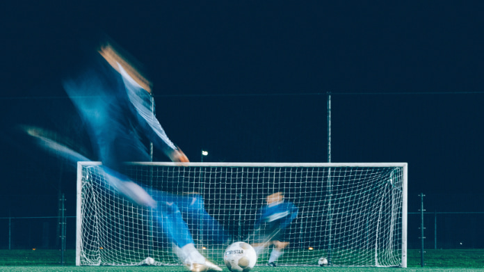 Fotbollsspelare tar sats för att skjuta straff mot mål under kvällsbelysning.