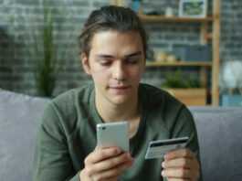 Ung man sitter i soffa och håller mobil och kreditkort när han gör ett köp online.