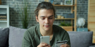 Ung man sitter i soffa och håller mobil och kreditkort när han gör ett köp online.