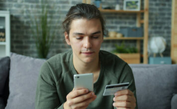 Ung man sitter i soffa och håller mobil och kreditkort när han gör ett köp online.