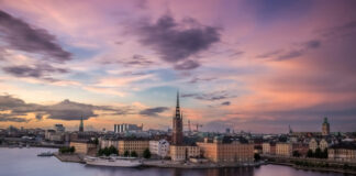 Stockholms silhuett vid solnedgång, med Riddarholmskyrkans torn i centrum och mjuka pastellfärger över himlen.