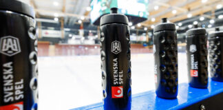 Vattenflaskor med Svenska Spel-logotypen uppställda vid sargen på en ishockeyrink.