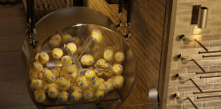 Lotterimaskin med gula numrerade bollar som snurrar i genomskinlig trumma.