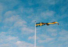 Svensk flagga som vajar i vinden mot en ljusblå himmel med lätta moln.