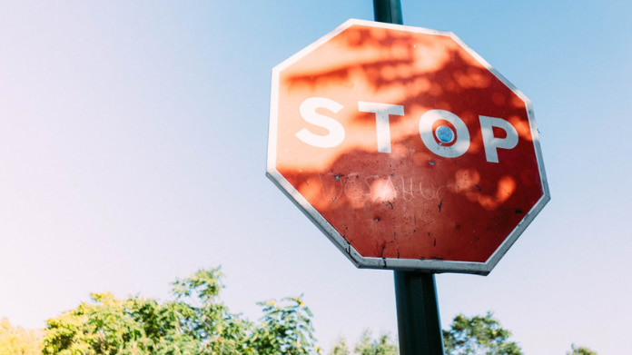 spelinspektionen-granskar-flera-sajter Röd stoppskylt med texten STOP mot blå himmel och träd i bakgrunden.