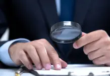 Så granskar Spelinspektionen nya aktörer på spelmarknaden Person i kostym granskar dokument med förstoringsglas