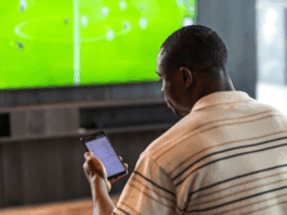 Person följer fotboll på tv och kollar på live betting odds i mobilen