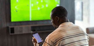 Vad händer när ett spelbolag stänger marknader i förtid? Person följer fotboll på tv och kollar på live betting odds i mobilen