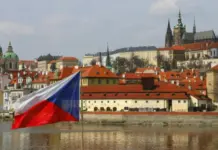 Tjeckien förlorar 147 miljoner kronor i månaden till olagligt spel – Sverige varnas Tjeckiens flagga vid flod med stadssiluett och historiska byggnader i Prag i bakgrunden.